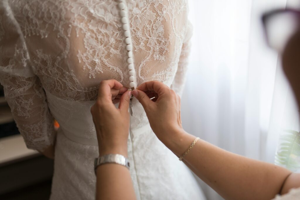 A bride getting her dress adjusted by a family member indoors, highlighting a touching wedding preparation moment.