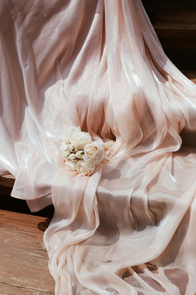 A delicate arrangement of white roses on elegant pink silk fabric, perfect for wedding themes.
