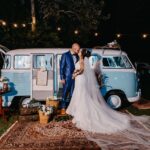 A bride and groom share a kiss by a vintage van in a romantic nighttime outdoor wedding setup.
