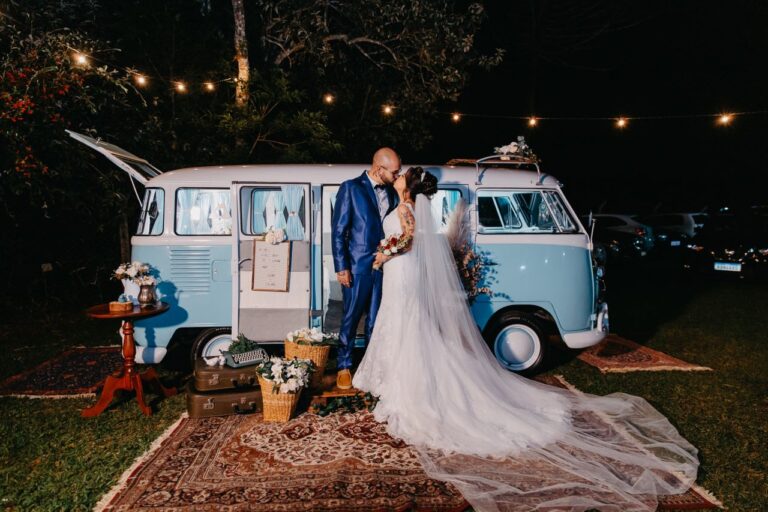 A bride and groom share a kiss by a vintage van in a romantic nighttime outdoor wedding setup.